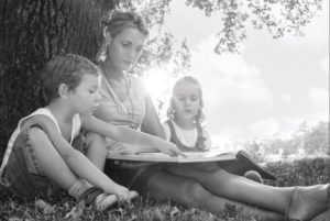 a women is reading a book to 2 children under a tree